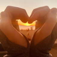 heart-shaped hands framing a Hawaiian sunset